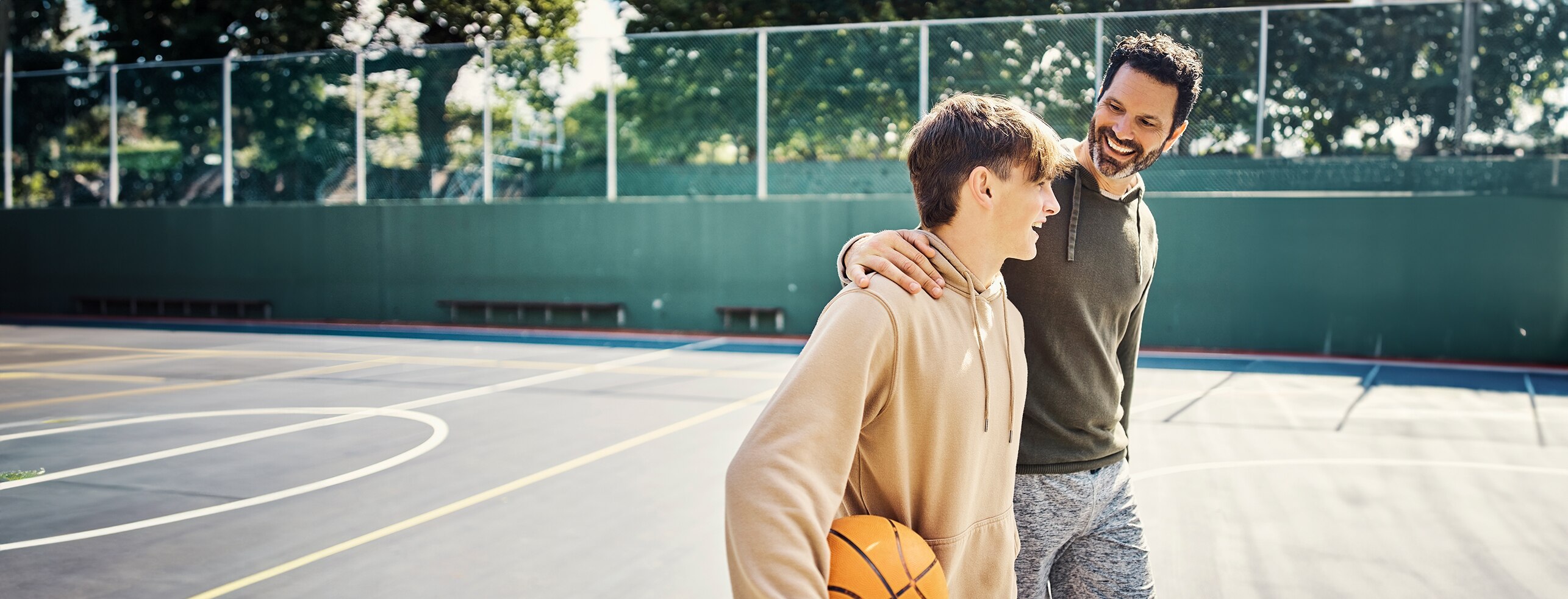 un père tenant l’épaule de son fils sur un terrain de basket