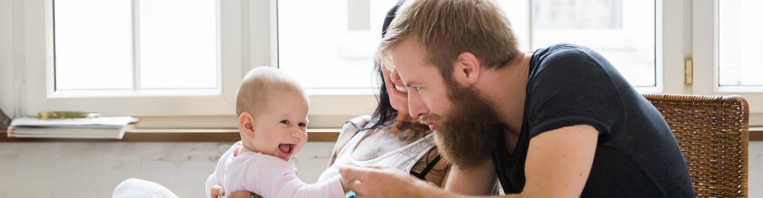 des parents et leur bébé sur les genoux sont à table avec une tablette