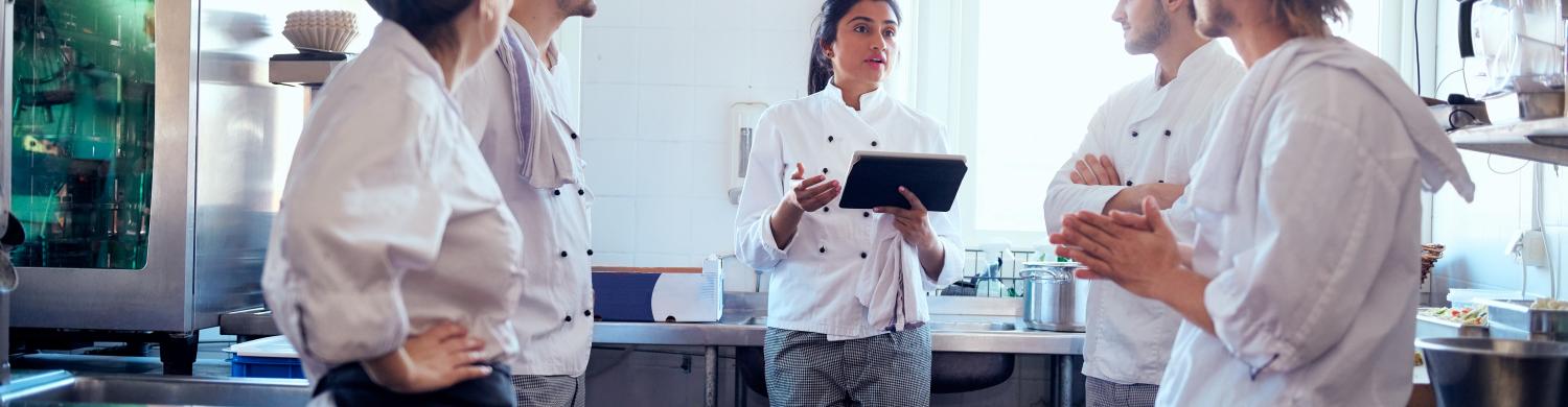 une équipe de cuisiniers dans une cuisine collective écoutent une personne