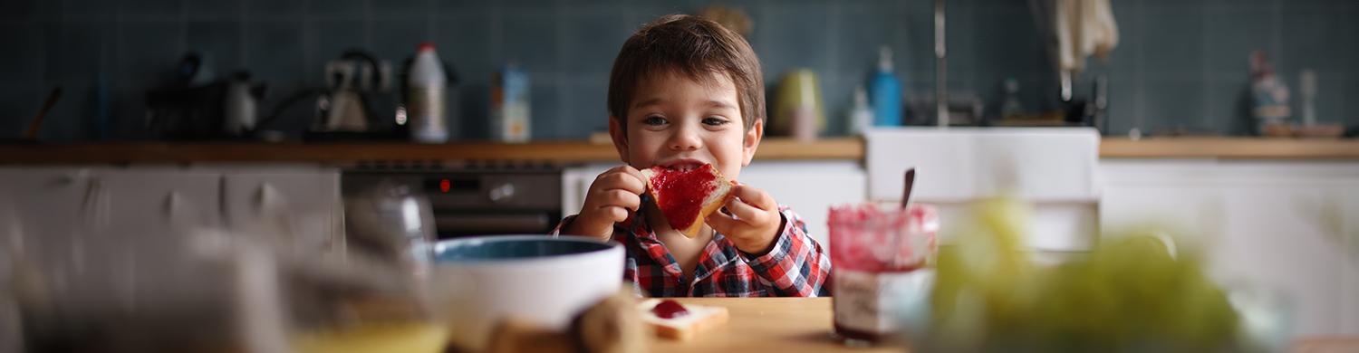 un enfant mange une tartine de confiture au petit-déjeuner