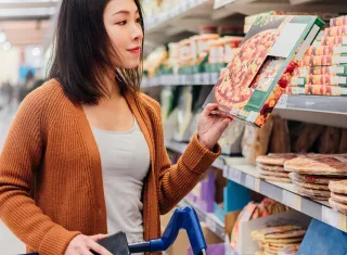 une femme choisit une pizza dans un rayon de supermarché