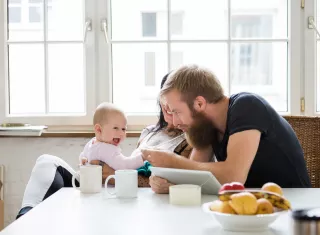 des parents et leur bébé sur les genoux sont à table avec une tablette