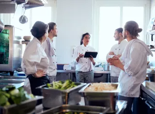 une équipe de cuisiniers dans une cuisine collective écoutent une personne