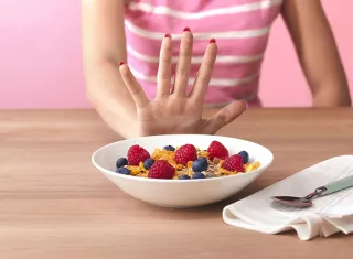 une  main qui repousse un bol de céréales et fraises 