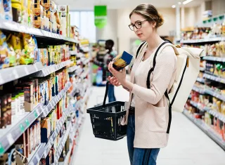 une dame avec des lunettes dans un rayon de supermarché qui regarde le dos d’un produit